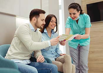 dental team member explaining the cost of dental implants to two patients