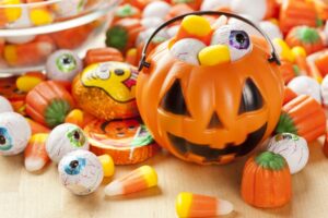 Pumpkin-shaped Halloween bowl surrounded by candy