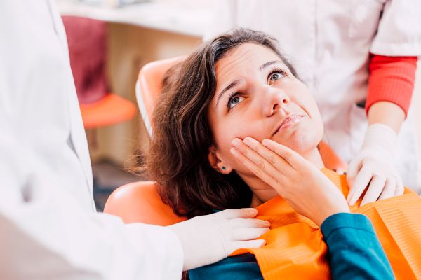 A woman in a dental chair holding her jaw
