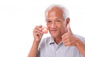 Older man holding dentures and giving thumbs-up.